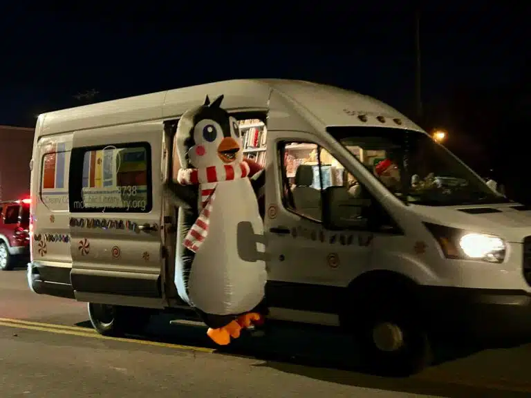 Photo of the library's bookmobile with a person in a penguin costume