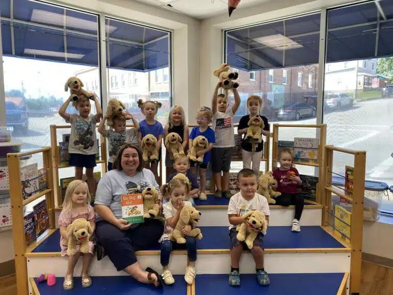 Picture shows children sitting and standing on a stage holding stuffed dog puppies.