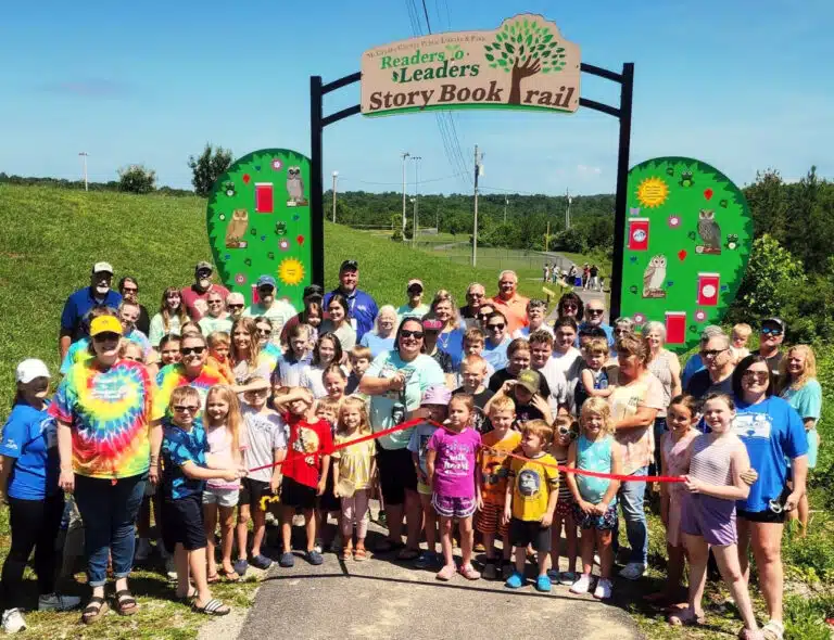 A crowd is gathered to cut a ribbon to open Storybook Trail